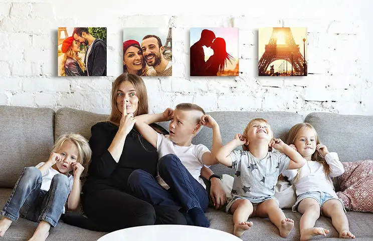 Mama und vier kleine Kinder sitzen auf dem Sofa vor vier Fotoleinwänden